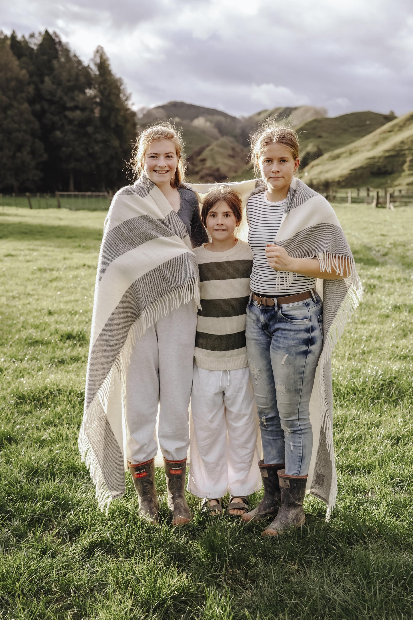 Three people standing in a grassy field with mountains in the background