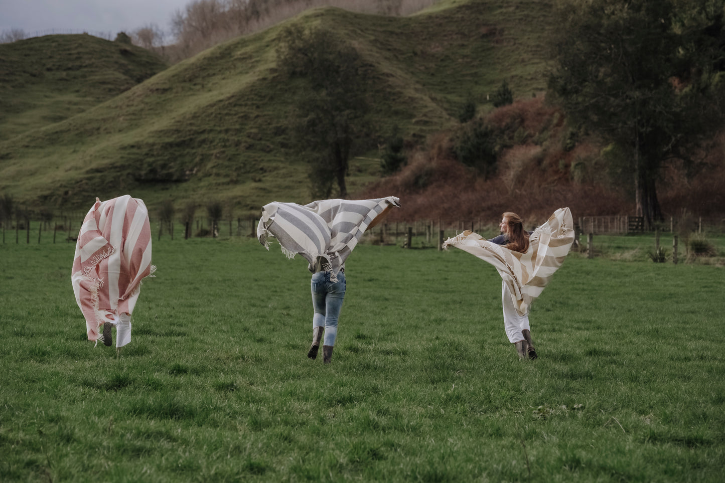 Three people with large fabric wings in a grassy field with rolling hills in the background