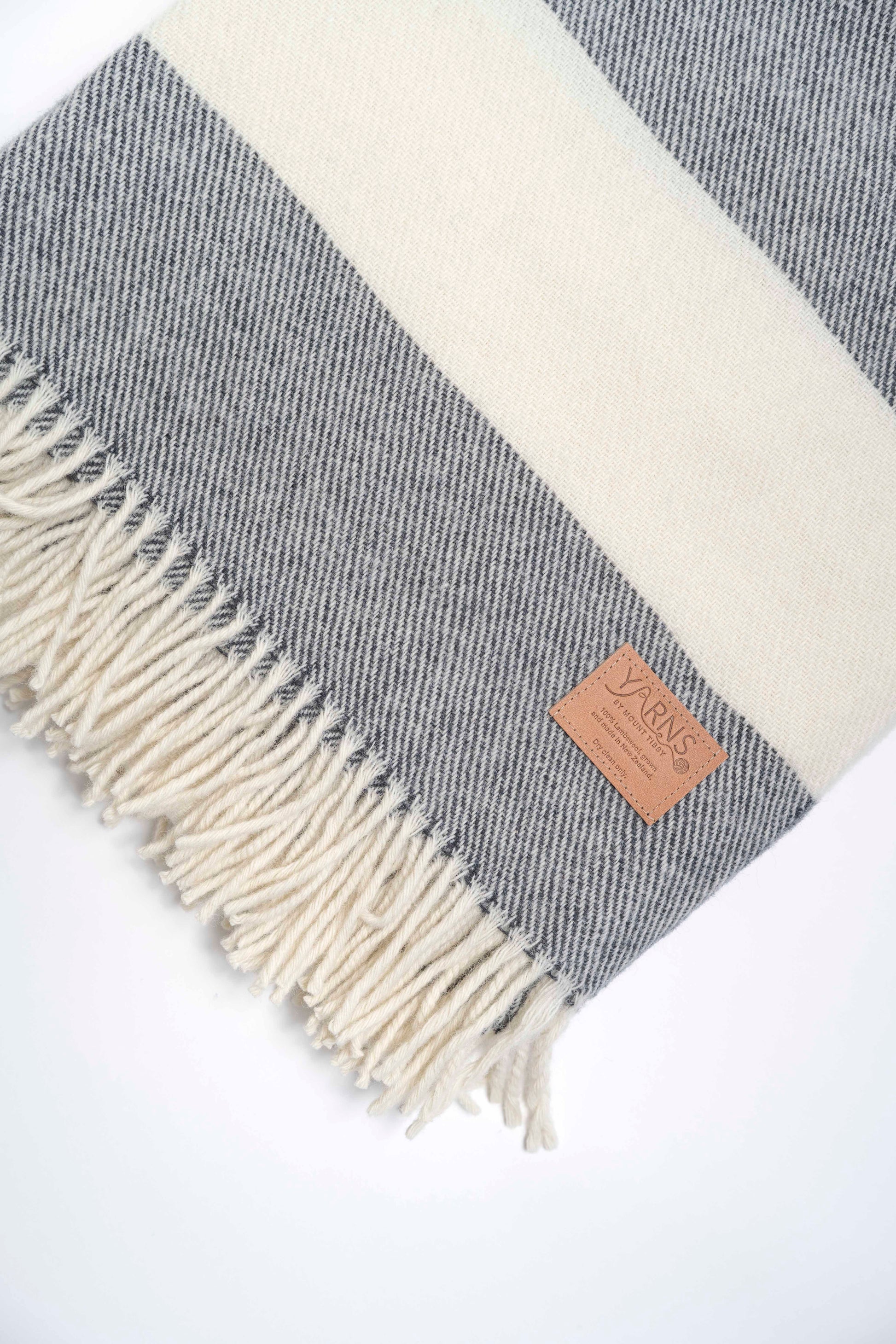 Gray and white striped blanket with fringes and a brand label on a white background