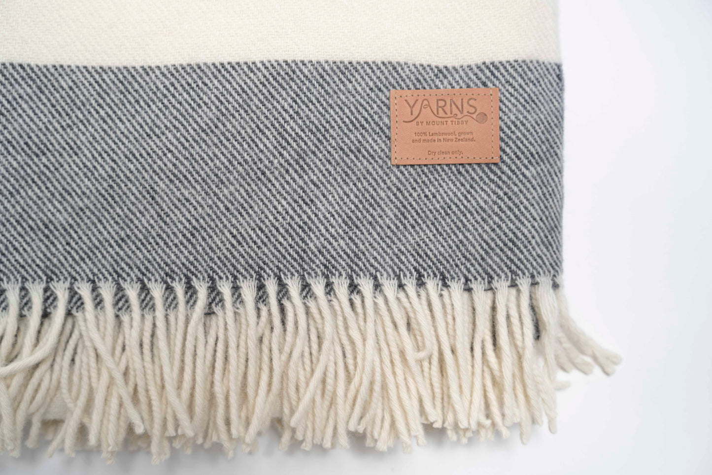 Charcoal and white striped blanket with fringes and a visible leather brand label on a light background
