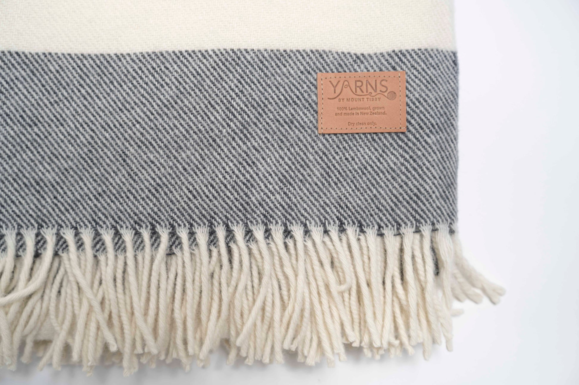 Charcoal and white striped blanket with fringes and a visible leather brand label on a light background