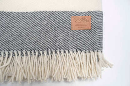 Charcoal and white striped blanket with fringes and a visible leather brand label on a light background